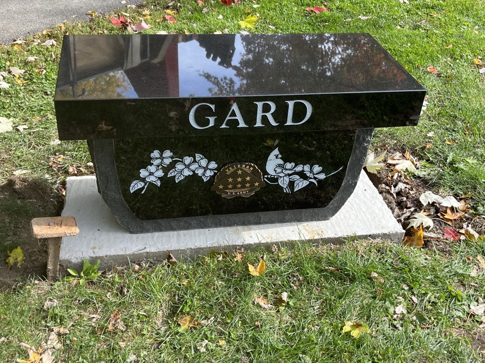 Black granite memorial bench with a rock pitched apron, etched dogwood and a bronze US Army veteran medallion