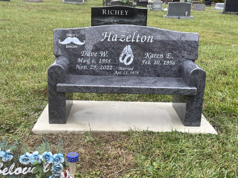 Blue grey granite memorial bench with a full back, arms, etched wedding rings and a small trade emblem