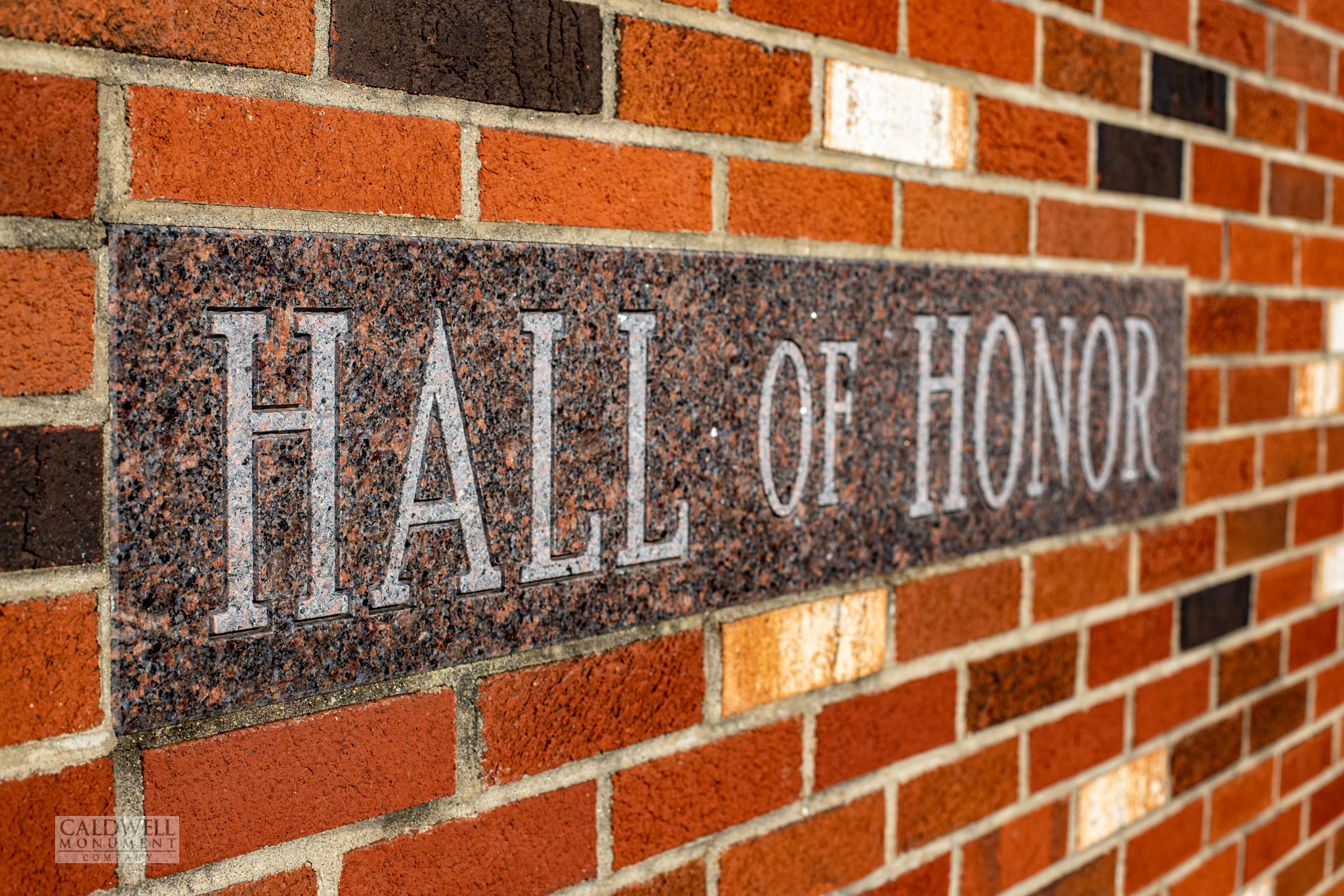 Carved granite Hall of Honor lintel set flush into a red brick wall, letters cut deep and left unpainted