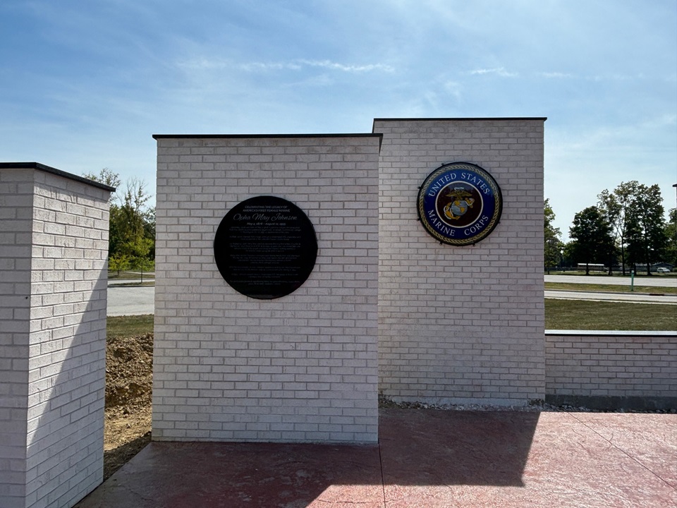 White brick memorial wall carrying a large round bronze plaque and a painted United States Marine Corps seal