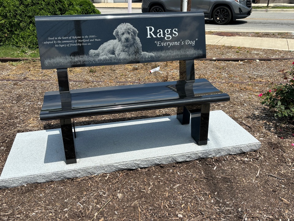 Black granite public bench with a full back, carrying a laser etched portrait of a dog and an inscription