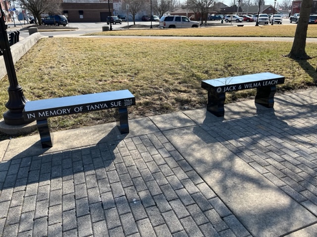 Two black granite memorial benches with curved legs set on a brick plaza at the courthouse