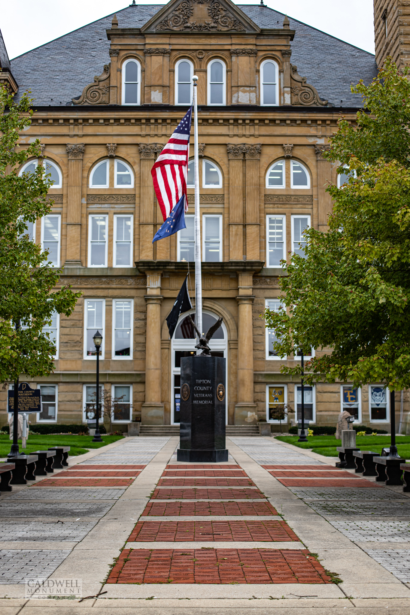 Black granite veterans memorial obelisk topped with a bronze eagle, standing on a brick walk in front of the Tipton County courthouse