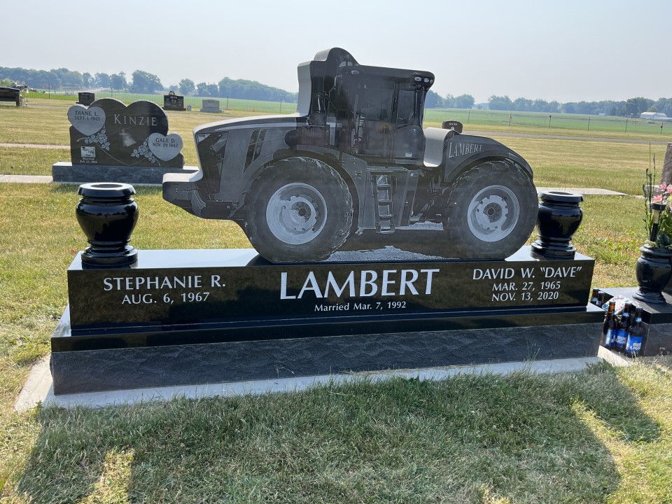 Black granite memorial cut to the silhouette of a tractor, standing on a polished black base with two vases