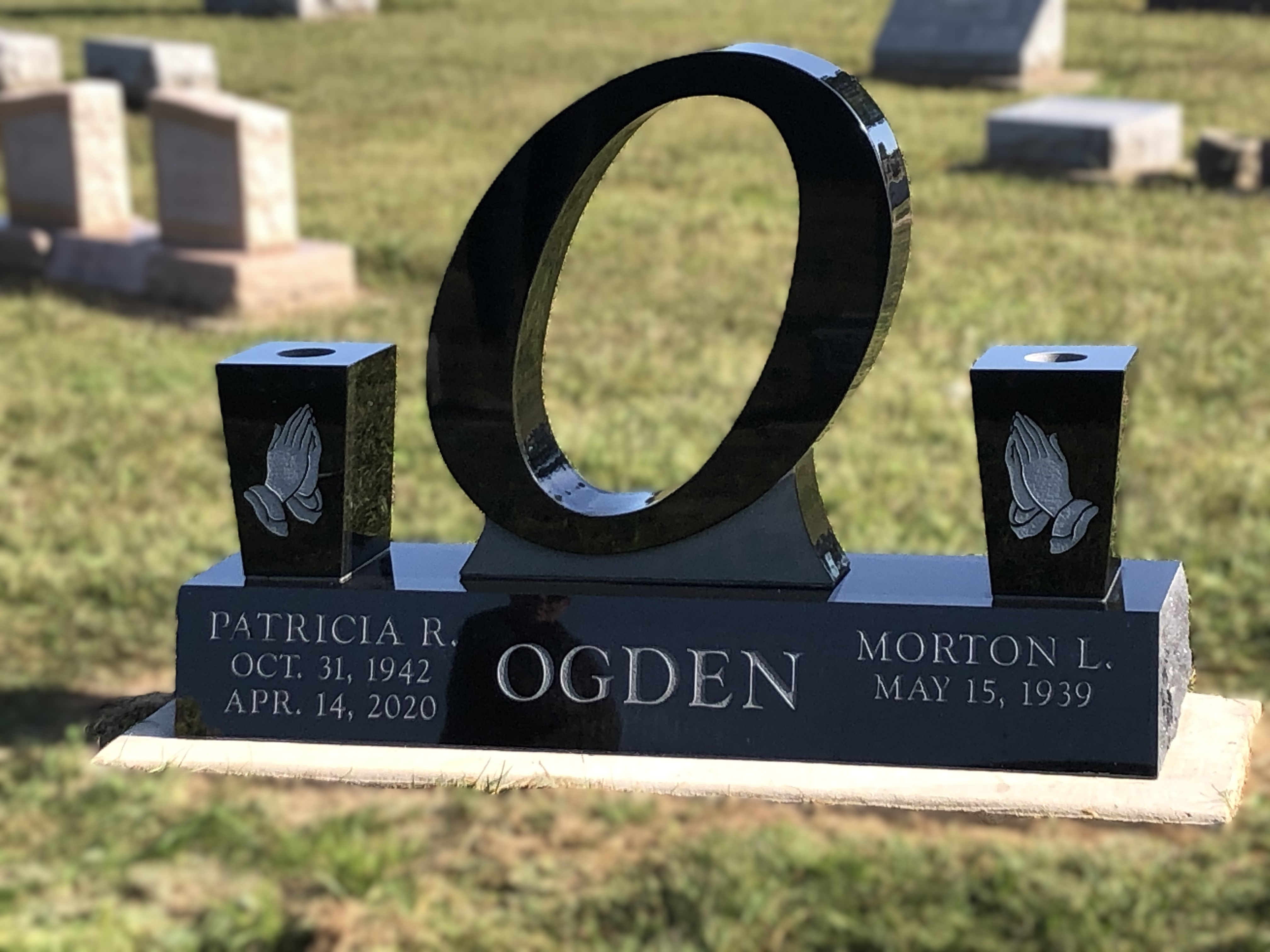 Polished black granite companion memorial cut as a large open ring, with two praying hands pillars either side