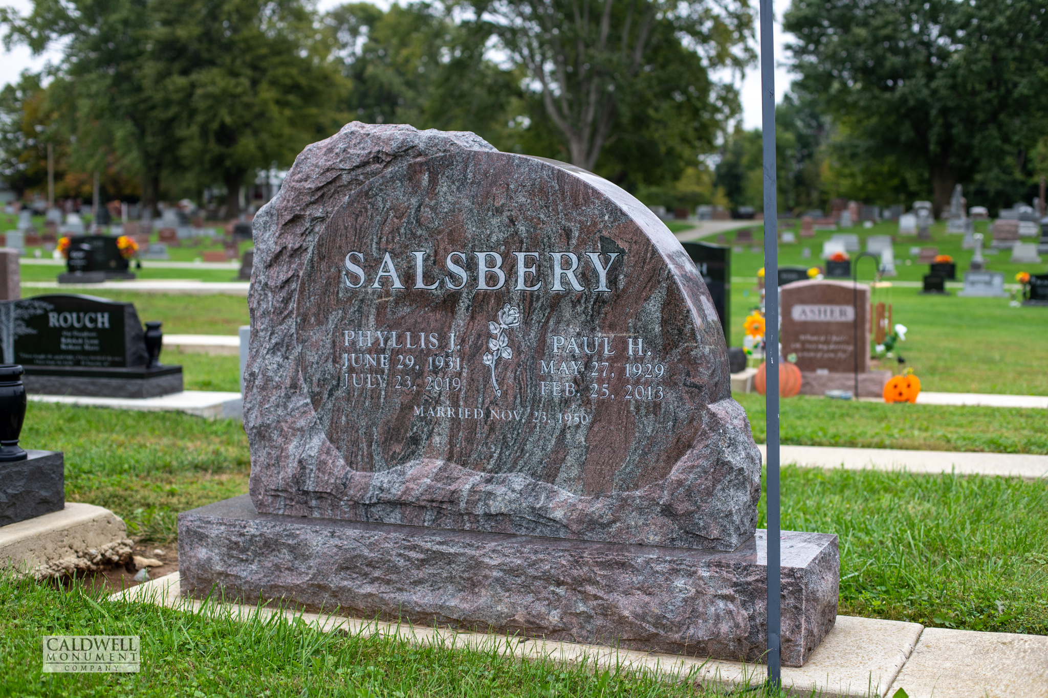 Rough hewn boulder shaped memorial in figured red granite with a polished oval face and a carved rose