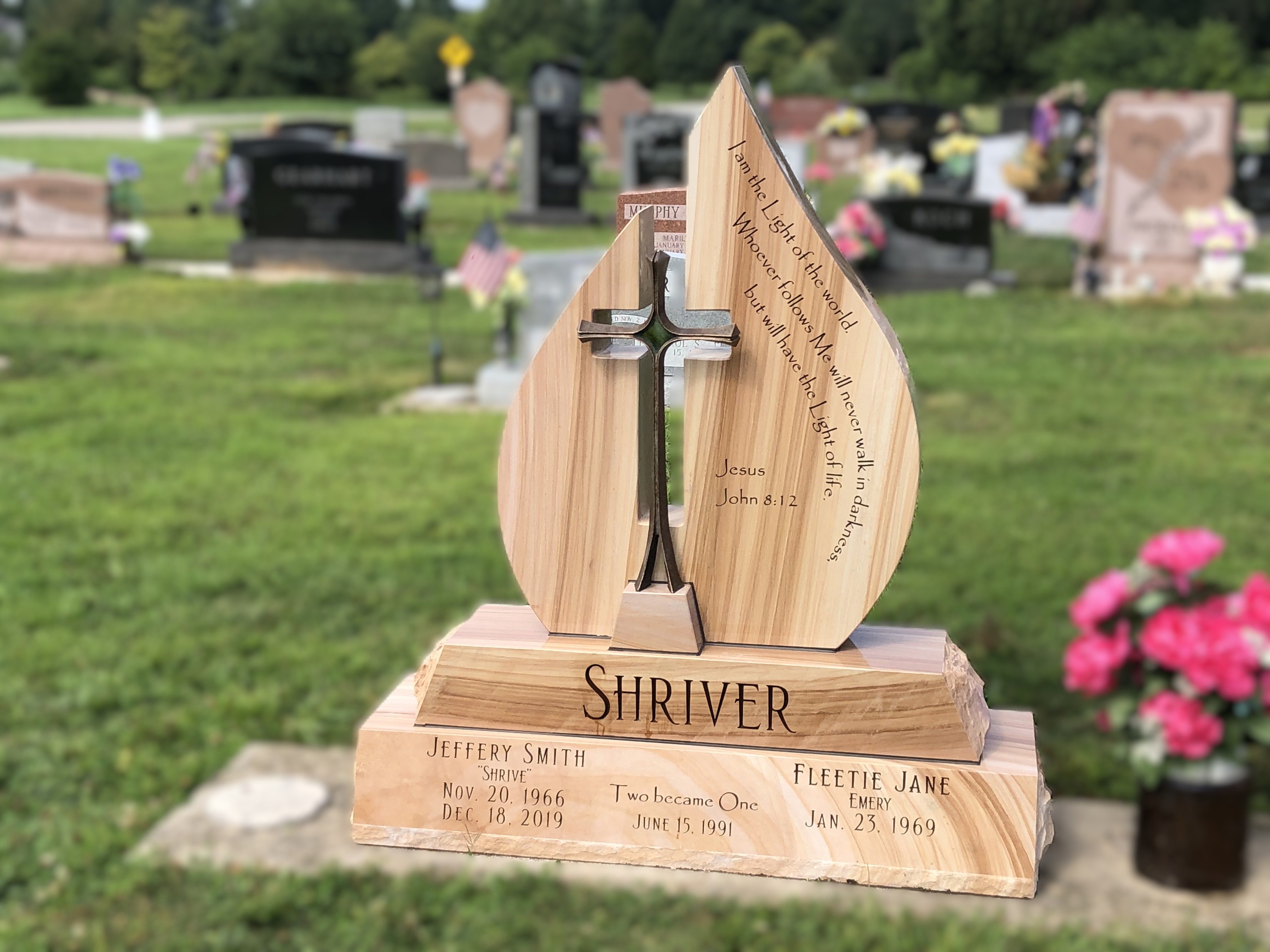 Woodgrain granite memorial cut as a flame and split down the middle around a standing bronze cross