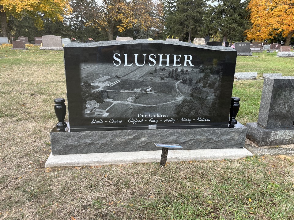 Black granite upright memorial with an aerial view of a farm laser etched across the full face, with two black granite vases