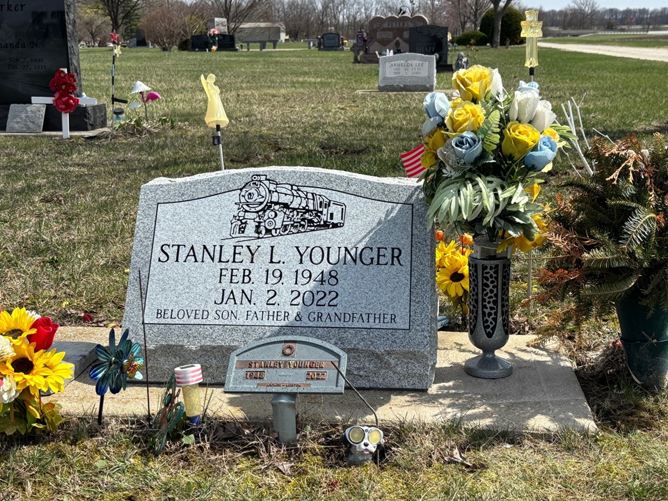 Grey granite slant marker with a steam locomotive etched above the lettering, with a companion flat marker in front